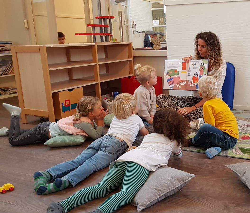 kinderen die in een kring rondom een medewerker zit van de peuteropvang die aan het voorlezen is bij SKH Stichting kinderopvang huizen