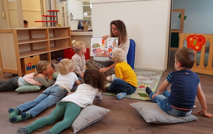 kinderen die in een kring rondom een medewerker zit van de peuteropvang die aan het voorlezen is bij SKH Stichting kinderopvang huizen