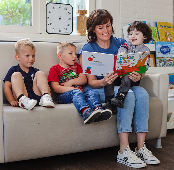 Drie kinderen die met een medewerker aan het lezen zijn bij het kinderdagverblijf van SKH stichting kinderopvang huizen