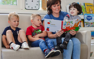 Drie kinderen die met een medewerker aan het lezen zijn bij het kinderdagverblijf van SKH stichting kinderopvang huizen