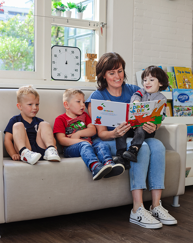 Drie kinderen die met een medewerker aan het lezen zijn bij het kinderdagverblijf van SKH stichting kinderopvang huizen