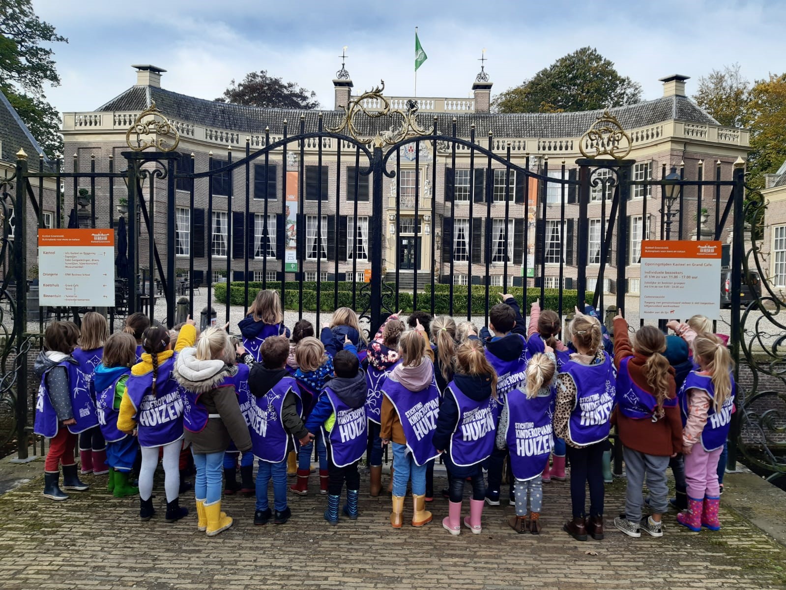 De kinderen die in SKH hesjes voor het hek van kasteel groeneveld staan